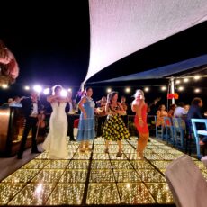 The bride and several friends stand on the optional LED dance floor on the rooftop of La Sirena Puerto Morelos. A mariachi band plays music and serenades them in the background.