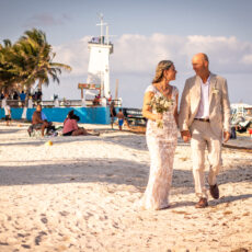 A newly married couple walk on the busy beach in Puerto Morelos, surrounded by other beachgoers and fisherman - the quintessential Puerto Morelos experience.