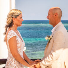 A couple hold hands during their wedding ceremony on the rooftop of La Sirena Puerto Morelos, overlooking the lighthouse and the ocean in the background.