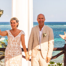 A bride triumphantly raises her wedding bouquet next to her groom just after finishing their wedding ceremony at La Sirena Puerto Morelos.