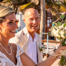 The bride leads the charge to the beach with her bouquet held high as the groom smiles broadly.