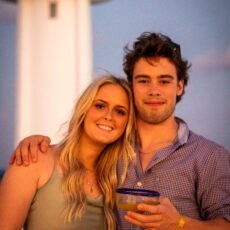 A young couple stands in front of the Puerto Morelos lighthouse on the rooftop of La Sirena Puerto Morelos during a wedding reception organized by Let's Marry in Mexico.