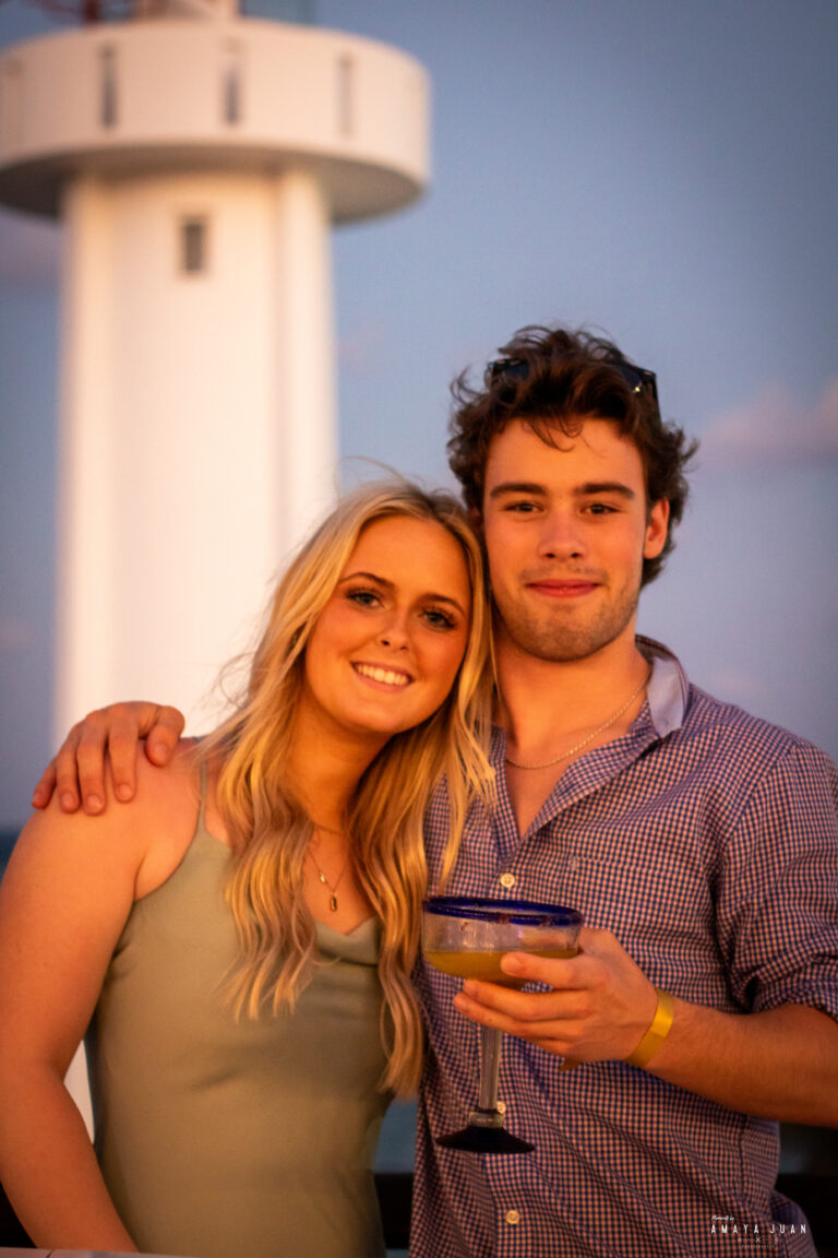A young couple stands in front of the Puerto Morelos lighthouse on the rooftop of La Sirena Puerto Morelos during a wedding reception organized by Let's Marry in Mexico.